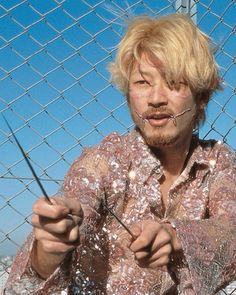 a man holding scissors in front of a chain link fence with barbed wire behind him