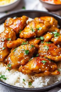 chicken wings with sesame seeds on top of white rice in a black bowl, ready to be eaten