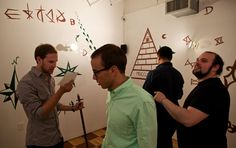 three men standing in an art gallery looking at artwork on the wall and writing on the walls