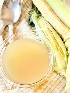 a glass bowl filled with liquid next to corn on the cob