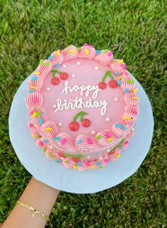 a pink birthday cake sitting on top of a white plate in the middle of grass