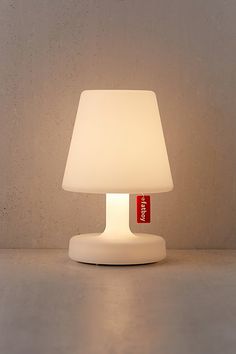 a white table lamp with a red tag on the base and a gray wall behind it