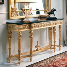 a gold console table with a mirror and lamp on it in front of a wall