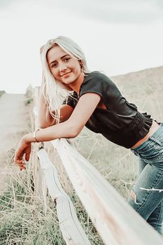 a woman leaning on a fence in the grass