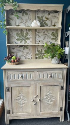 an old china cabinet with plants on top and wallpaper behind it in a room