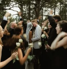 a group of people standing next to each other in front of trees and one person holding flowers