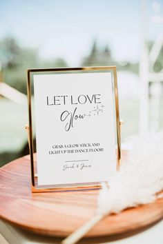 a sign that says let love grow on top of a wooden table with feathers around it