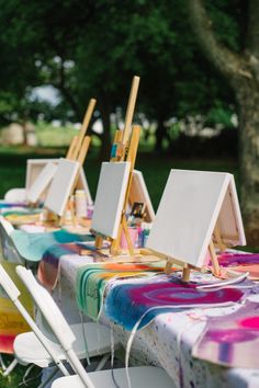 several easels are lined up on a table with colorful cloths and paintbrushes