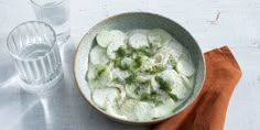 a bowl of cucumbers and water on a white table with an orange napkin