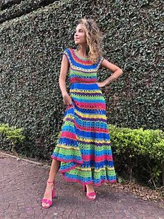 a woman standing in front of a hedge wearing a multicolored dress