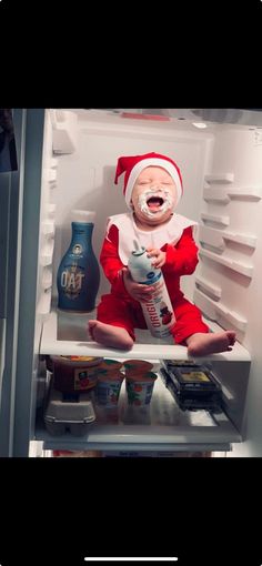 a baby dressed as santa claus sitting in an open refrigerator with milk and yogurt