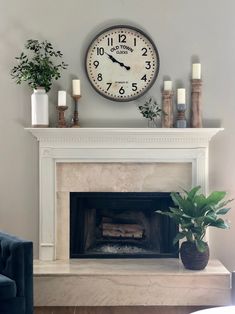 a clock above a fireplace with candles and plants on the mantels in front of it