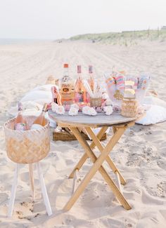 a picnic table on the beach with bottles and baskets full of food sitting on it