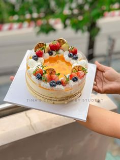 a person holding a cake with fruit on it