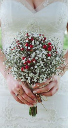 a woman in a wedding dress holding a bouquet of white and red flowers with her hands