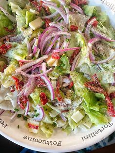 a salad with lettuce, red onions and cheese on it in a white bowl