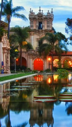 a large building with a pond in front of it and palm trees around it at dusk