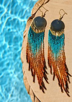 two pairs of beaded earrings sitting on top of a table next to a swimming pool