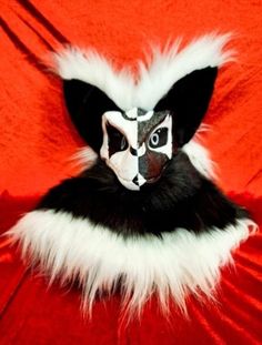 a cat in the hat mask on top of a red cloth covered bed with white and black fur