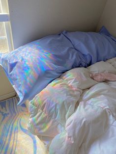 an unmade bed with white sheets and blue pillowcases in front of a window