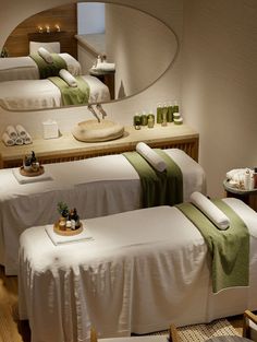 three white beds with green towels on them in a room next to a sink and mirror