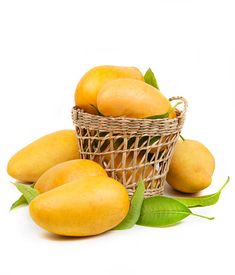 several mangoes in a wicker basket with green leaves on the side and white background