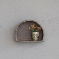 there is a vase with flowers in it on the wall above a shelf that has been made out of concrete