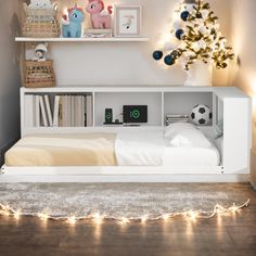 a white bed sitting under a christmas tree next to a shelf filled with books and toys