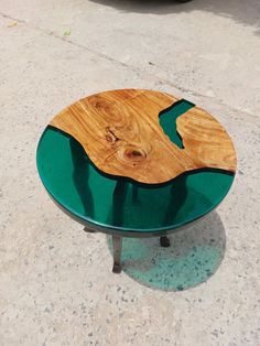 a wooden table with green glass top sitting on the sidewalk next to a parked car