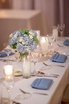 the table is set with blue napkins, silverware and white flowers in vases