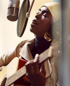 a woman sitting in front of a microphone while holding a guitar and singing into a microphone