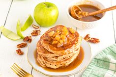 a stack of pancakes on a plate with caramel syrup and apples in the background