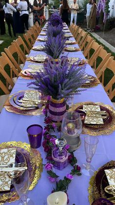 a long table is set with purple and gold plates, place settings, and flowers