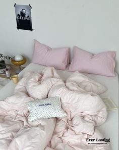 an unmade bed with pink sheets and pillows on it in a white walled room