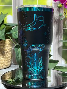 a glass cup with blue and black designs on it sitting on a table next to a potted plant