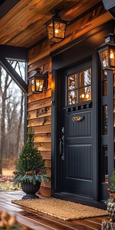 a black front door with two lights on it and a potted tree in the foreground