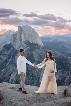 a pregnant couple holding hands while standing on top of a mountain