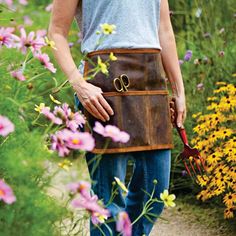 a man is holding a garden tool in his right hand and wearing a leather apron