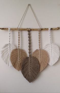 three different colored feathers hanging from a wooden stick on a wall with white and brown accents