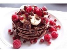 a stack of chocolate pancakes topped with bananas and raspberries