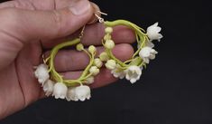 a hand holding a pair of earrings with white flowers on the inside and green stems