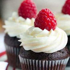 three cupcakes with white frosting and raspberries on top are sitting on a plate