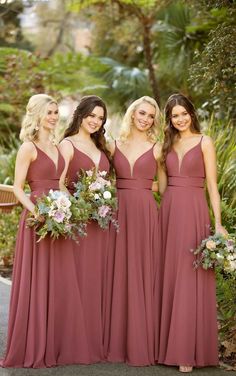 three bridesmaids in maroon dresses posing for the camera with bouquets and greenery