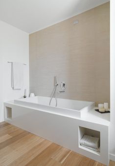 a white bathtub sitting on top of a wooden floor next to a shower head