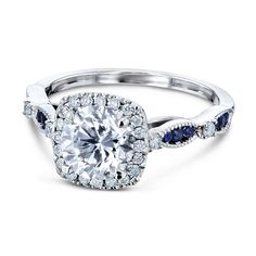 1-1/3 CTW Round Diamond, Blue Sapphire, and Accent Diamond Engagement Ring in 14k White Gold Natural 1ct diamond center stone, diamond halo, blue sapphire accented band. One Round Diamond (1ct) 24 Round Diamonds (1/5ct TDW) 12 Round Blue Sapphires (1/8ct TGW) 14k Gold Design Features: Milgrain Edging, Pinched Shank, Mixed Stones View the Collection Cushion Moissanite Version Round Moissanite Version Matching Wedding Band Cushion Moissanite Engagement Ring, Engagement Rings Sale, Gold Anniversary Rings, Blue Moissanite, Blue Sapphire Ring, Sapphire Engagement Ring Blue, Moissanite Wedding Rings, Sapphire Engagement Ring, Ring Blue