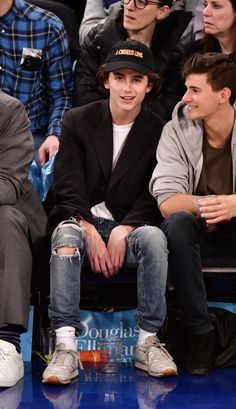 two young men sitting next to each other in front of a crowd at a basketball game