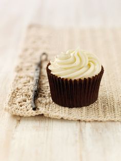 a cupcake with white frosting sitting on top of a table next to a pen