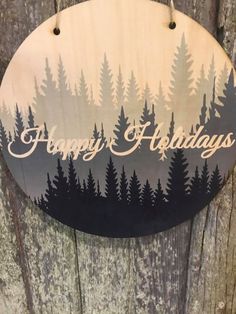 a wooden sign that says happy holidays hanging on a tree trunk with pine trees in the background