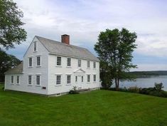 a large white house sitting on top of a lush green field next to a lake