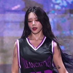 a woman with long black hair wearing a purple and black basketball uniform on the runway